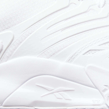 Close-up of a white Reebok Phase EVO Tennis Shoe, showcasing textured, layered materials and the embossed Reebok logo on the side. Smooth curves and raised patterns highlight its durable tennis shoe design.