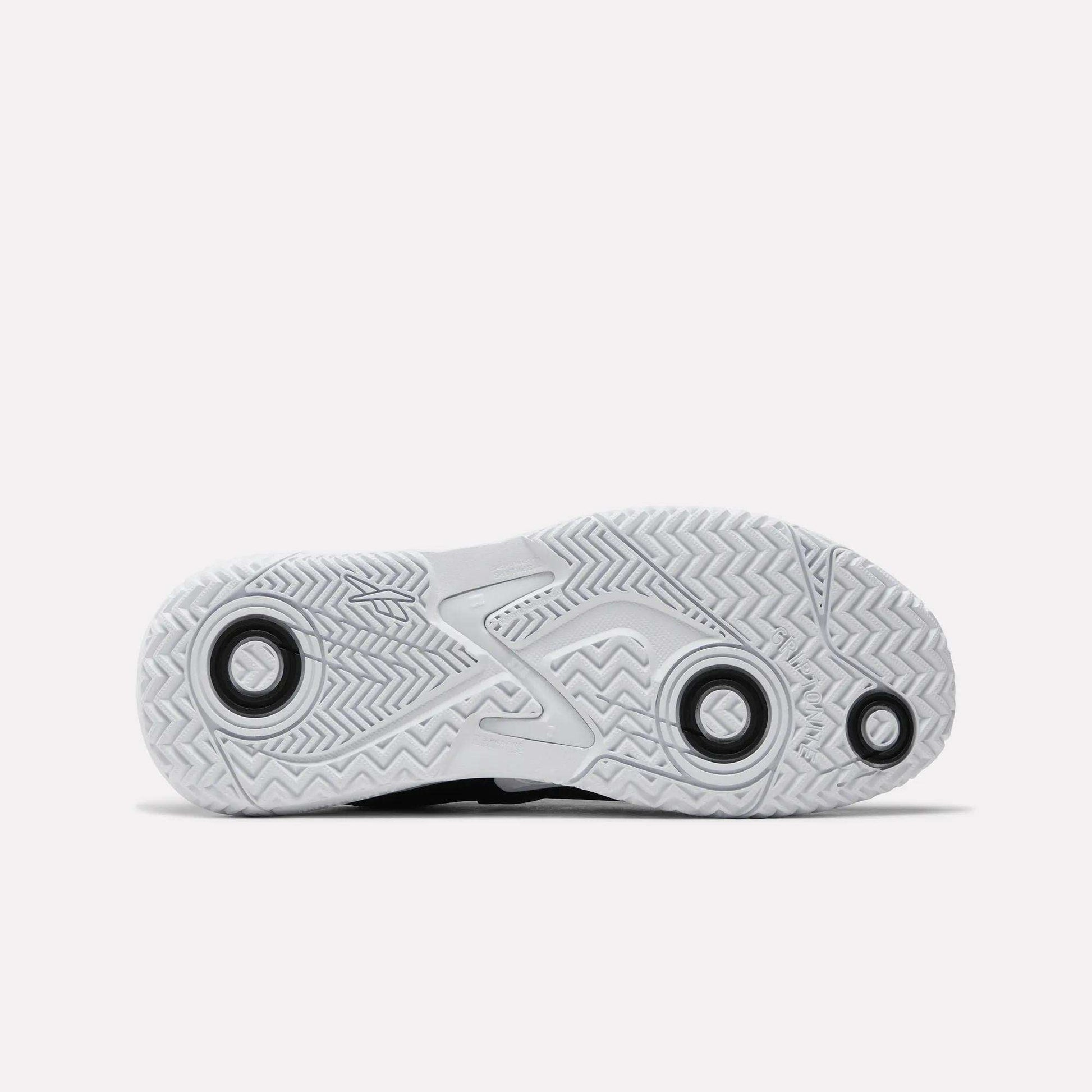 The image features the sole of Reebok Women's Phase Evo Tennis Shoes, displaying a herringbone tread, circular grip accents, and a raised midsection for durability, all set against a plain white background.