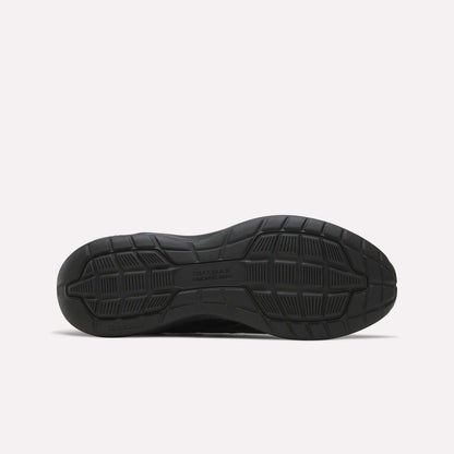 The image displays the black rubber sole of the Reebok Men's Walk Ultra 7 DMX Max Shoes, positioned flat to showcase its tread pattern. The sole includes textured grip sections and features DMX MAX and Reebok embossed on it, emphasizing the advanced DMX cushioning technology characteristic of these cushioned walking shoes.