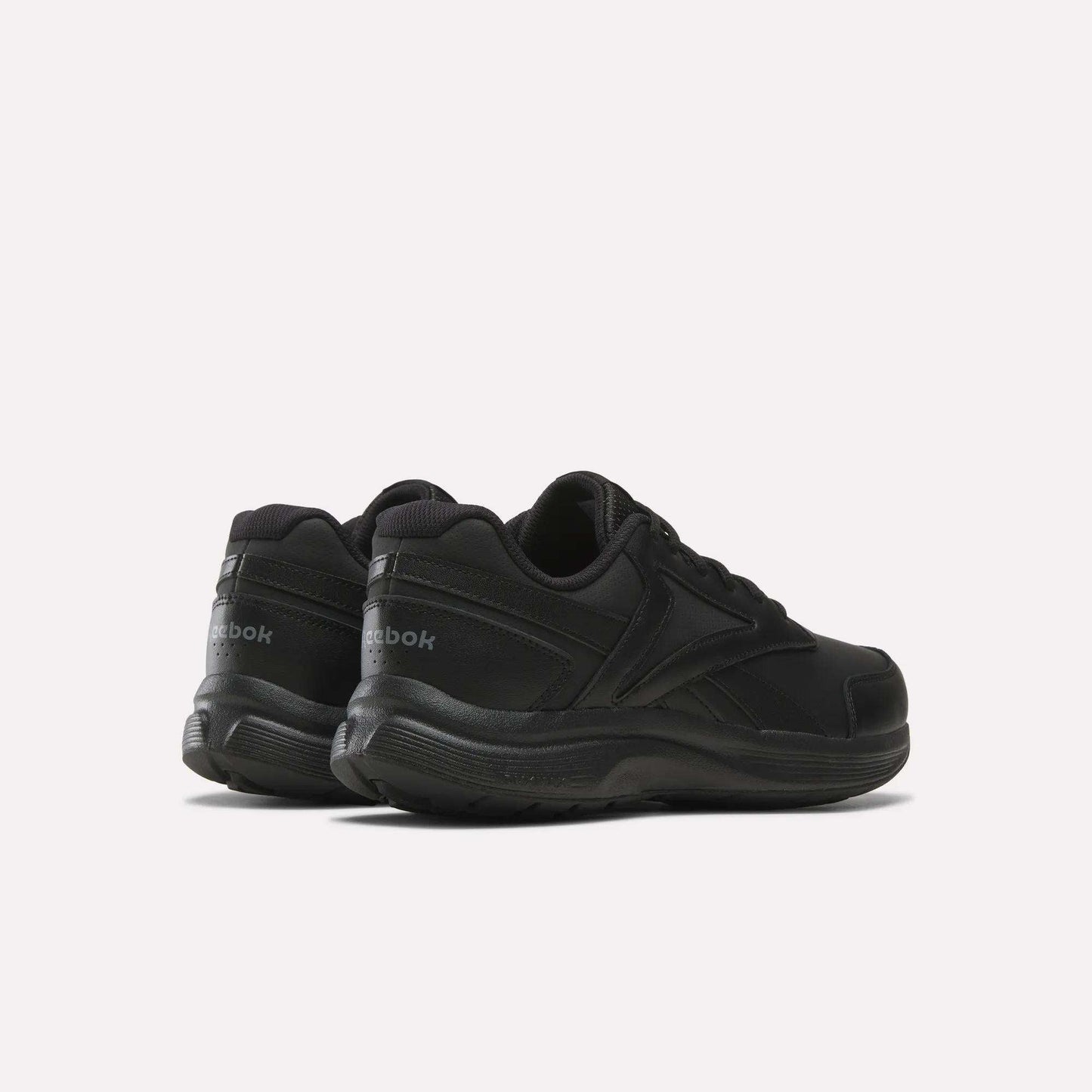 A pair of Men's Walk Ultra 7 DMX Max Shoes - Wide 4E by Reebok are displayed on a white background, angled with the heels facing the camera and toes pointing outward. These black wide-fit walking shoes feature DMX cushioning, delivering comfort and support for everyday wear.