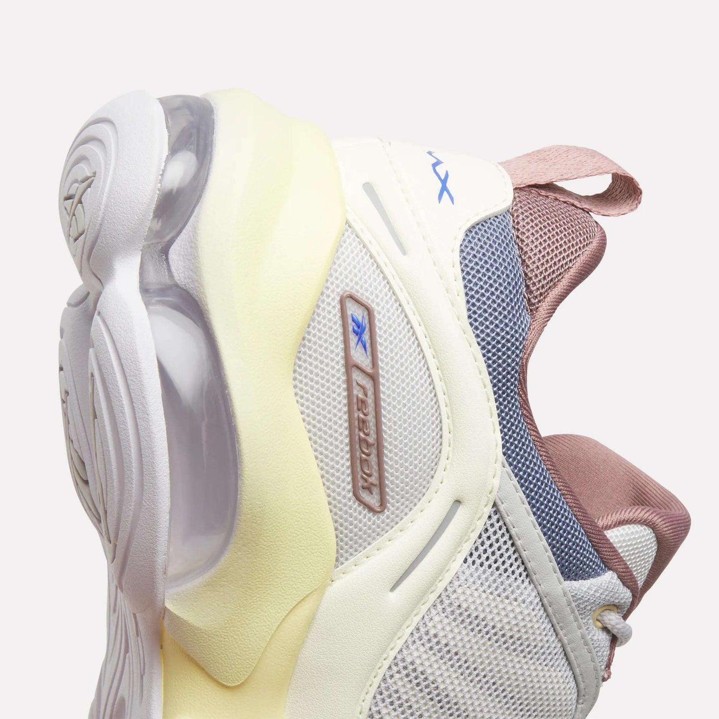 Close-up of the Women's DMX Series 3000 Training Shoes by Reebok, showcasing a stylish combination of white, cream, and pink hues with mesh and rubber textures, visible air cushioning in the sole powered by DMX 3 Technology, and a blue Reebok logo on the side.