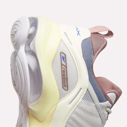 Close-up of the Women's DMX Series 3000 Training Shoes by Reebok, showcasing a stylish combination of white, cream, and pink hues with mesh and rubber textures, visible air cushioning in the sole powered by DMX 3 Technology, and a blue Reebok logo on the side.
