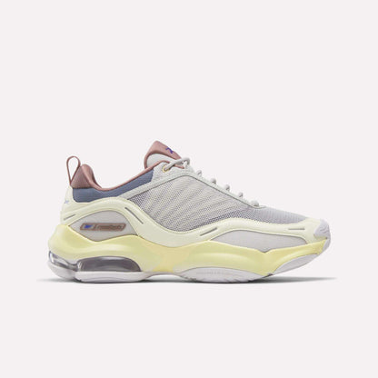 Introducing the Reebok Women's DMX Series 3000 Training Shoes—a stylish athletic shoe featuring a cream-toned New Grey mesh upper accented with Raw Yellow and Hazy Blue details. Designed with layered textures, a translucent sole, and a chunky silhouette, these shoes combine modern aesthetics with the signature cushioned comfort of Reebok walking shoes.