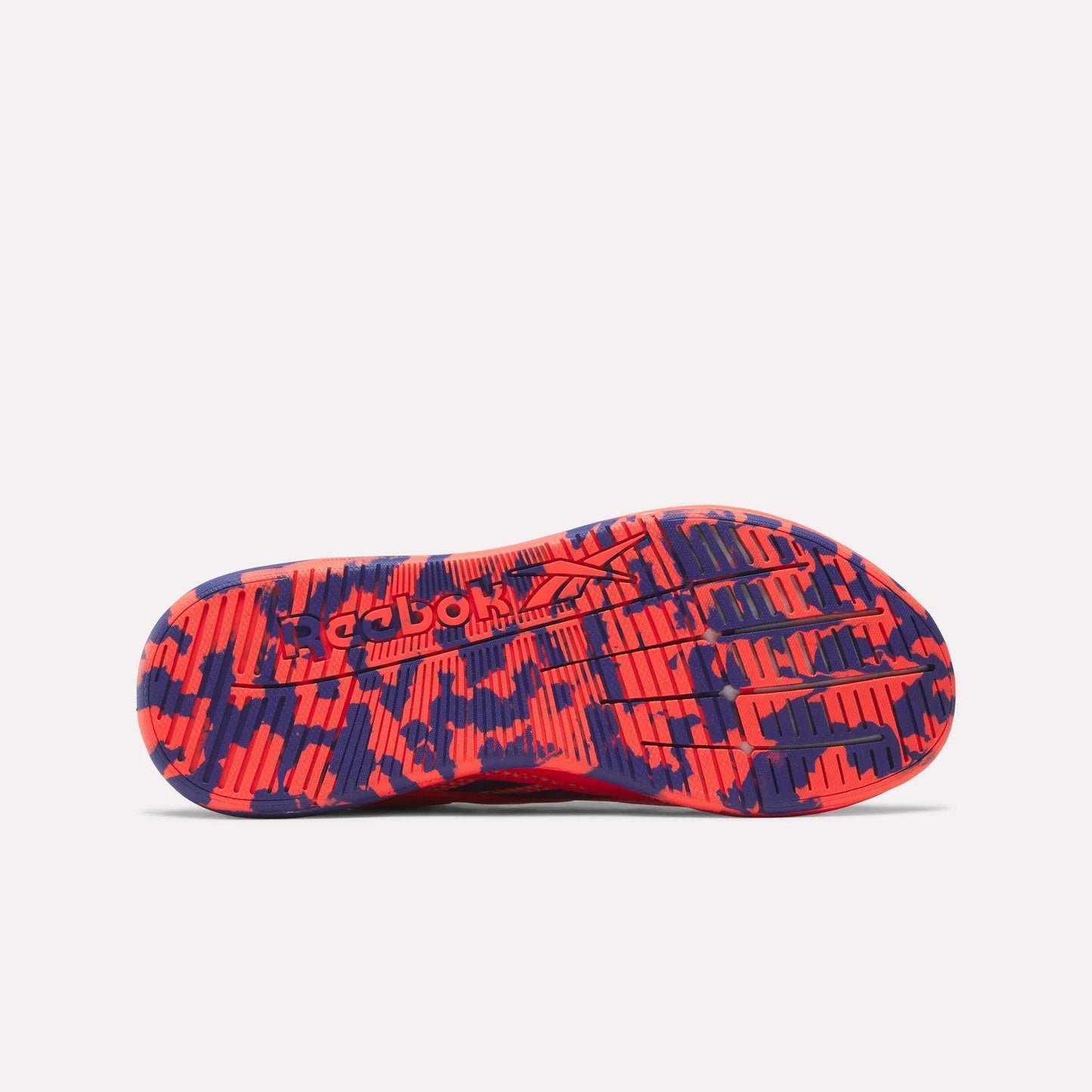 The image features the sole of a women's Reebok Nano X5 Edge Training Shoe with a striking red and navy camo pattern. The Reebok logo appears in the center, while grooved lines and textured areas deliver grip for intense training sessions.