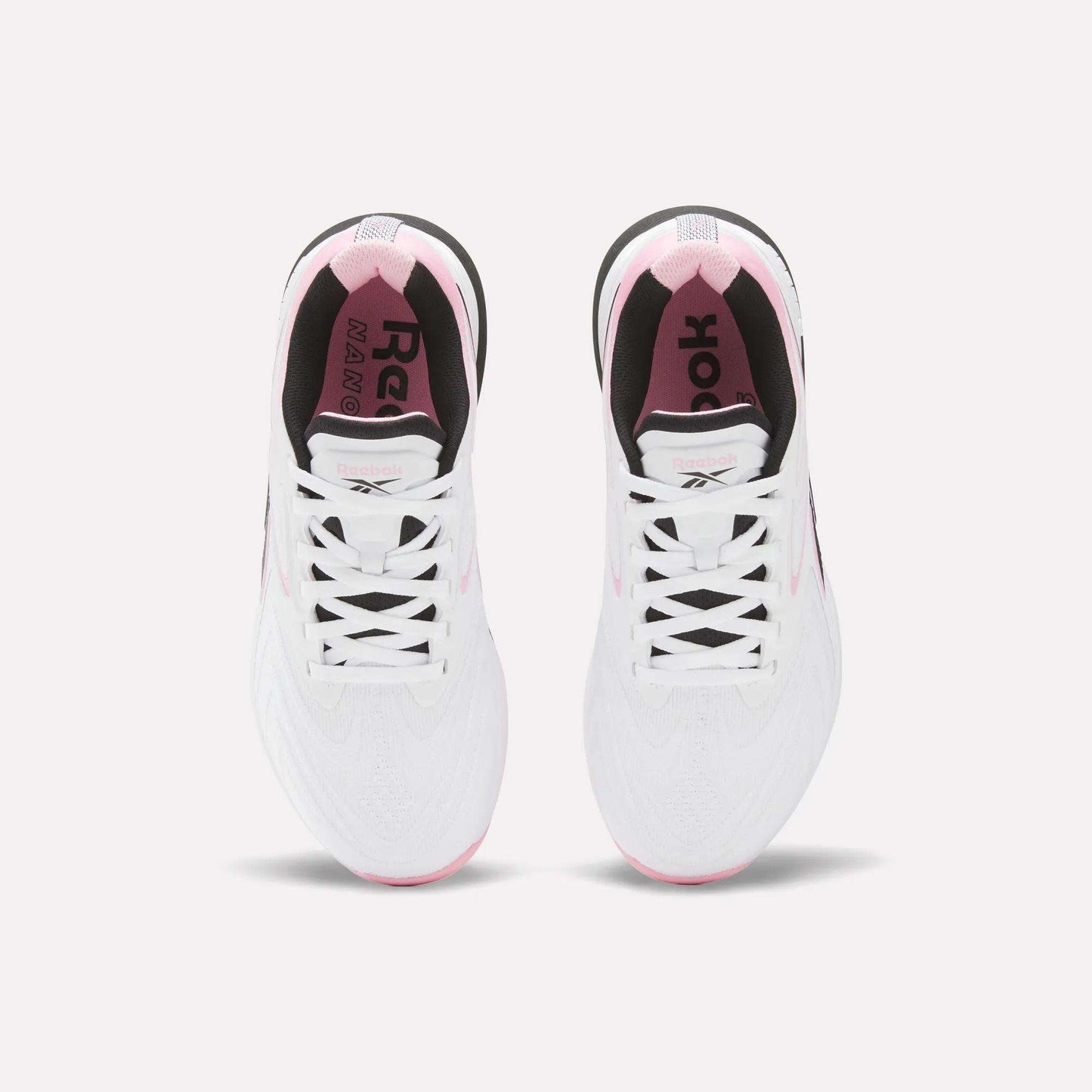 Top view of Reebok Women's Nano X5 Edge Training Shoes in white with pink accents, black inner lining, and visible laces, shown side by side on a light background.