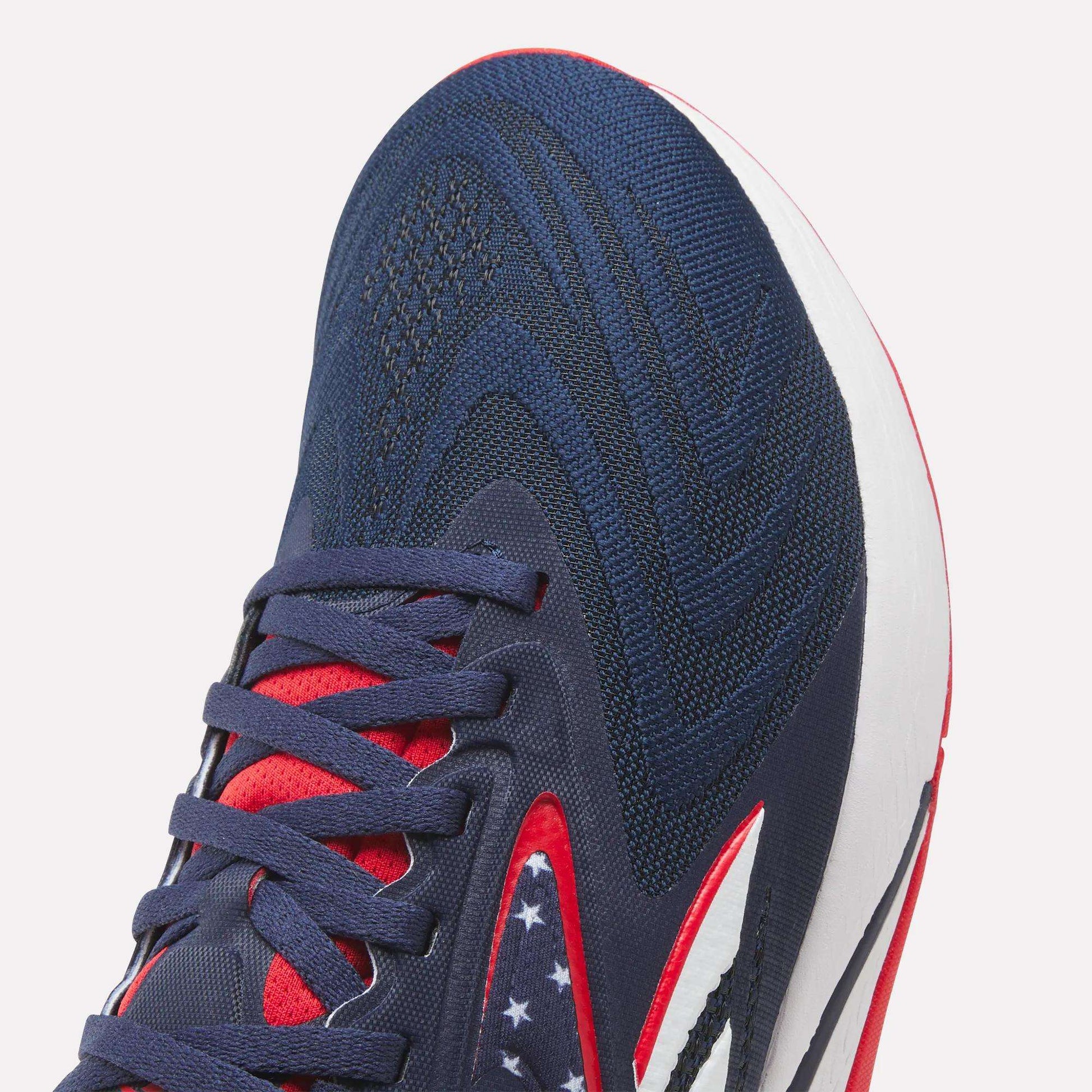 Close-up of Reebok Nano X5 Edge Training Shoes in navy with red and white accents, patterned laces, and white stars on a dark blue section. Featuring a Flexweave upper and white midsole for durability—ideal for precision training.