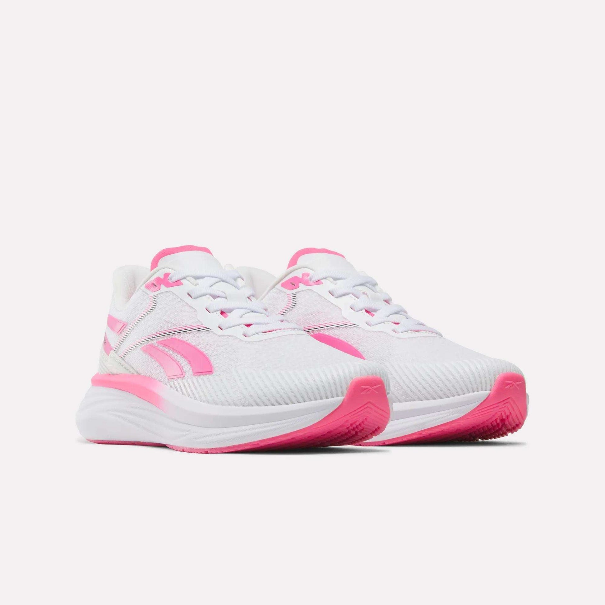 A pair of Women's Viva Speed Shoes by Reebok, these white athletic sneakers feature pink accents on the sides, laces, and soles. Designed as cushioned running shoes, they offer both comfort and support and are shown against a plain white background.