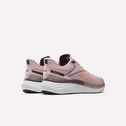 A pair of Reebok Women’s Viva Speed Shoes in pink and white is displayed against a plain white background, angled to highlight the side and back details. These cushioned running shoes offer a breathable design for comfort and support during everyday activities.