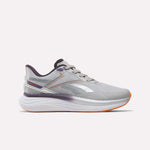 The Women's Viva Speed Shoes by Reebok feature a New Grey 1 upper with Phantom Purple and Alt Orange accents. Designed for both style and support, these athletic running shoes showcase the iconic Reebok logo on the side. A thick, white cushioned midsole provides superior comfort, while the shoes are photographed against a plain white background.