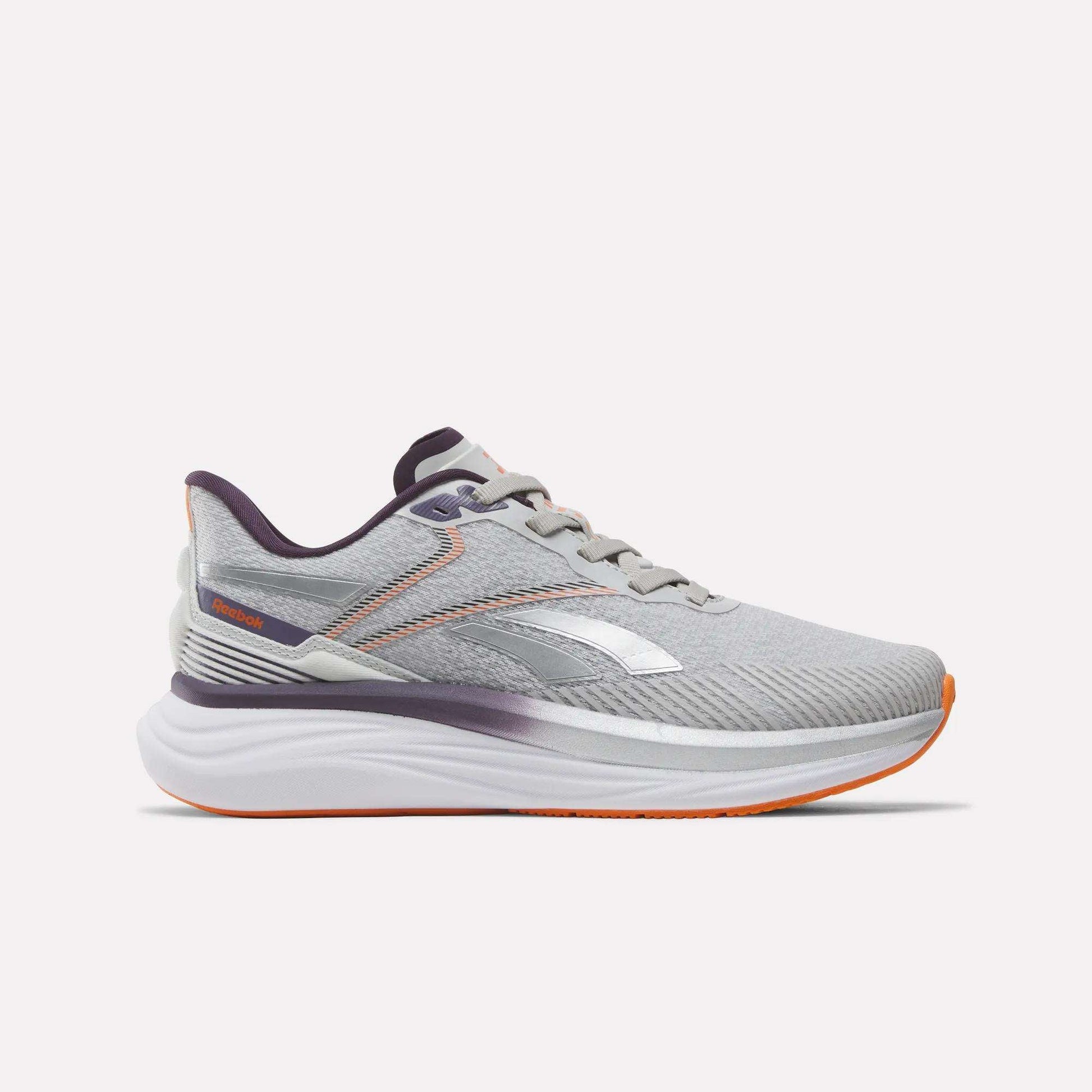 The Women's Viva Speed Shoes by Reebok feature a New Grey 1 upper with Phantom Purple and Alt Orange accents. Designed for both style and support, these athletic running shoes showcase the iconic Reebok logo on the side. A thick, white cushioned midsole provides superior comfort, while the shoes are photographed against a plain white background.