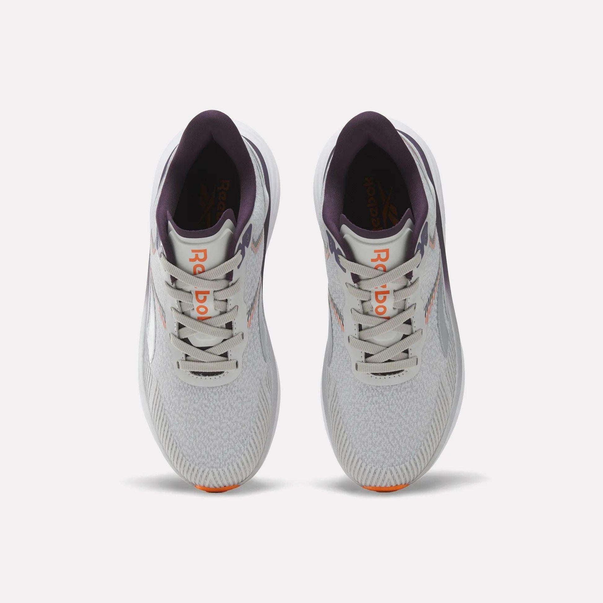 Top view of a pair of Reebok Women's Viva Speed Shoes in light gray with purple accents, featuring an orange logo on the tongue, white laces, and lightly patterned mesh uppers, placed side by side on a plain white background. These breathable running shoes offer a cushioned midsole for enhanced comfort with every stride.