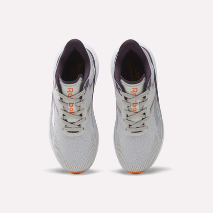 Top view of a pair of Reebok Women's Viva Speed Shoes in light gray with purple accents, featuring an orange logo on the tongue, white laces, and lightly patterned mesh uppers, placed side by side on a plain white background. These breathable running shoes offer a cushioned midsole for enhanced comfort with every stride.