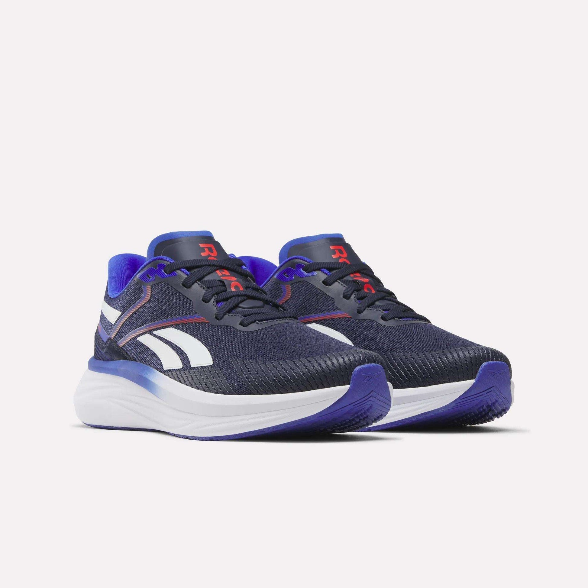 A pair of Men's Viva Speed Shoes by Reebok in navy blue, featuring white midsoles, purple accents, and white side stripes. These cushioned shoes provide comfort during daily runs and are designed with red R logos on the tongues and a textured toe area.