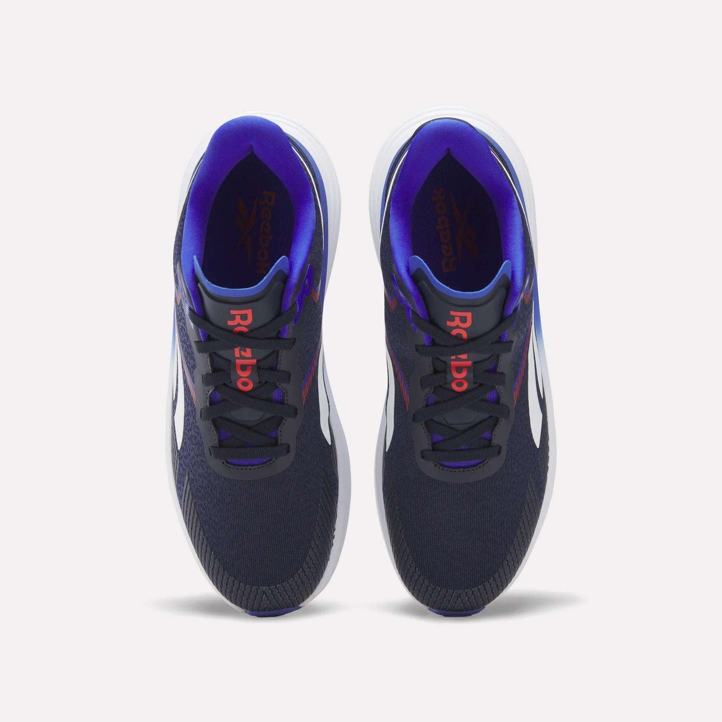 A pair of Reebok Men's Viva Speed Shoes in navy blue, featuring white soles, red Reebok logos on the tongues, and a purple inner lining, are displayed from a top view against a white background. Designed for both comfort and performance, these cushioned shoes are ideal for men seeking style and support.