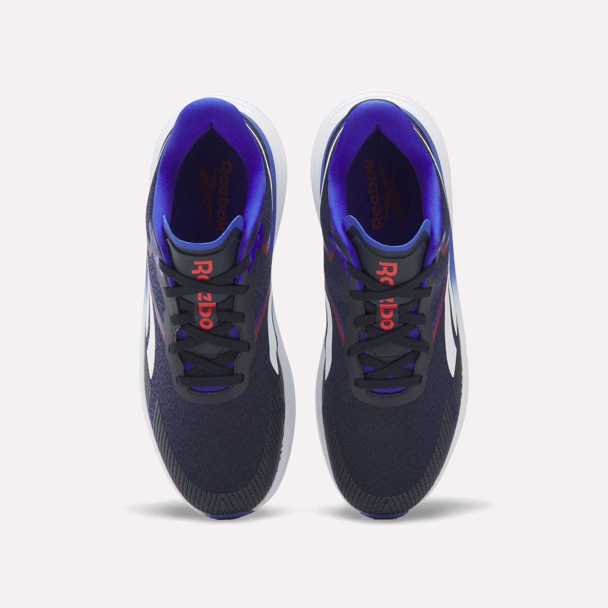 A pair of Reebok Men's Viva Speed Shoes in navy blue, featuring white soles, red Reebok logos on the tongues, and a purple inner lining, are displayed from a top view against a white background. Designed for both comfort and performance, these cushioned shoes are ideal for men seeking style and support.