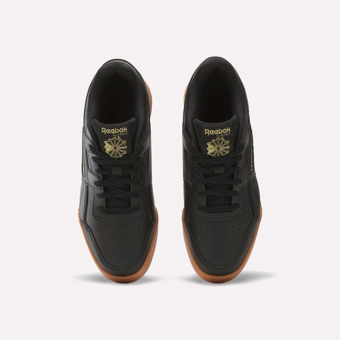 Top view of Reebok Workout Plus Shoes for big kids in black with brown gum soles, gold branding, and a star logo on the tongue, side by side on a white background—a sporty pick for juniors.