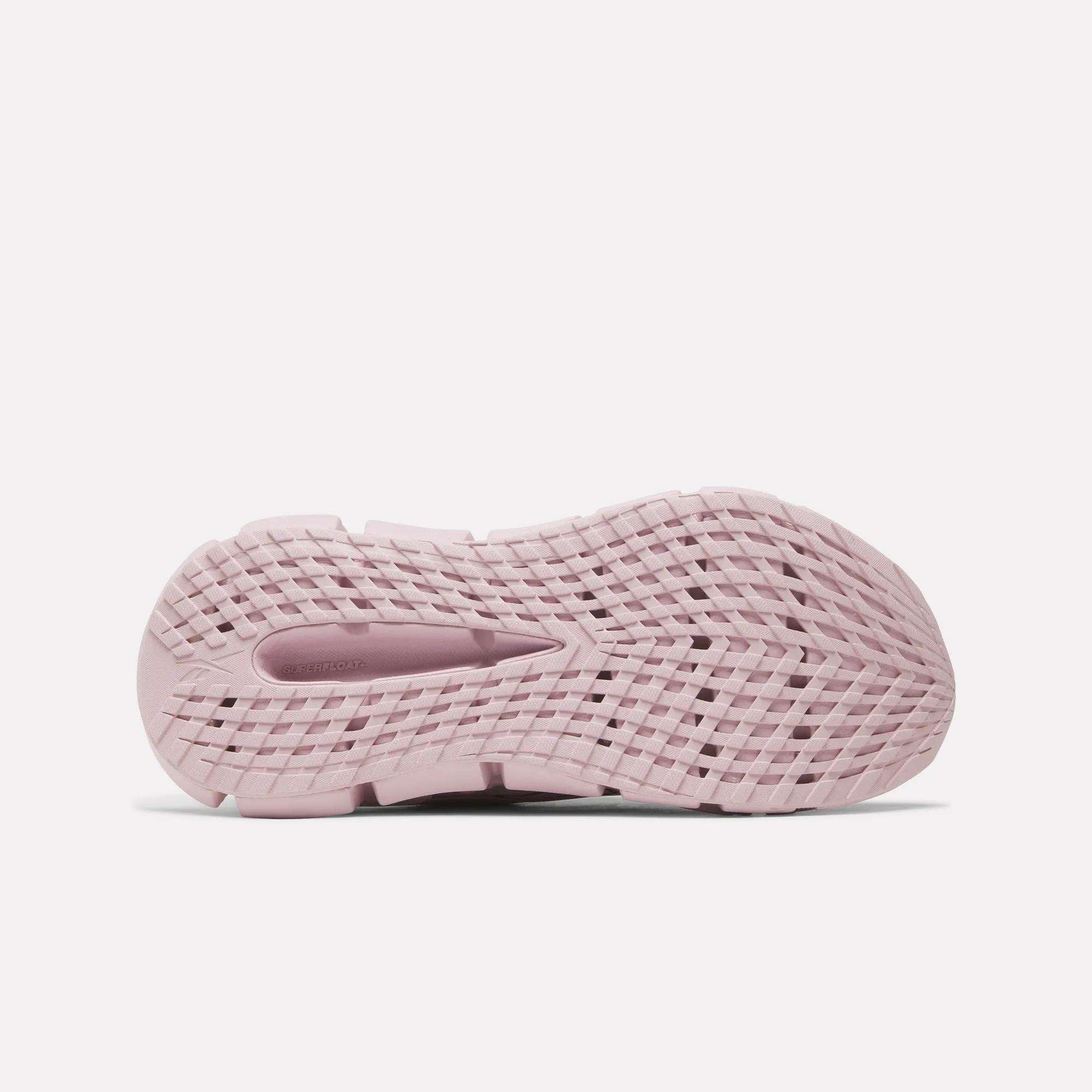 The image shows the bottom view of a pink Women's FloatZig 2 Running Shoe by Reebok, featuring a textured, grid-like sole pattern for grip and flexibility with Superfloat+ cushioning for enhanced comfort.
