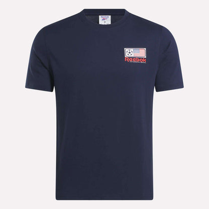 The Reebok USA Football T-Shirt is a navy blue, short-sleeve cotton jersey with a left chest patch featuring a soccer ball, American flag, red Reebok logo, and "International" text.