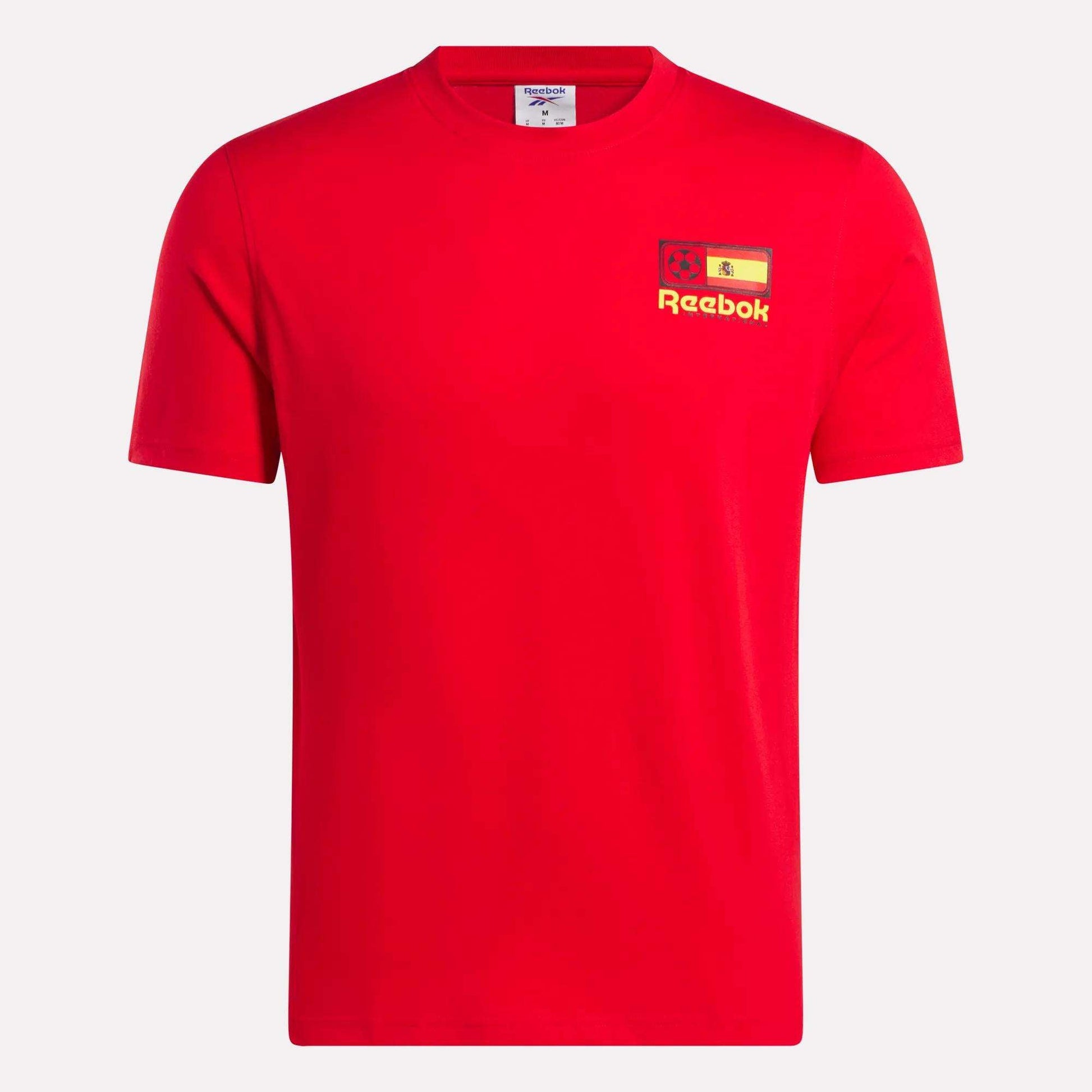 The España Football T-Shirt by Reebok is a plain red cotton tee with a small yellow Reebok logo, lion graphic, and the Spanish flag on the left chest, featuring a classic crew neck and short sleeves.