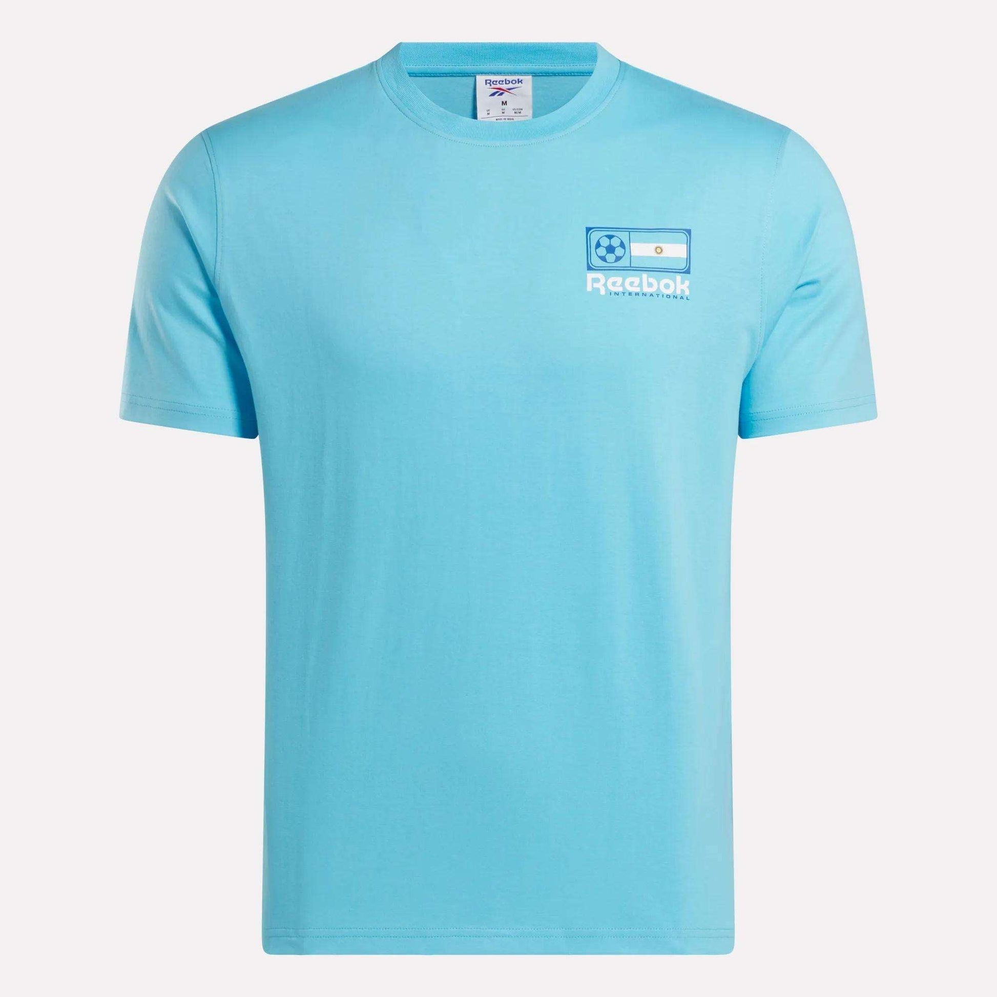 The Reebok Argentina Football T-Shirt is a light blue cotton tee with a small left chest logo featuring the Argentina flag, soccer ball, and "Reebok" in white—a great choice for Argentina fans.