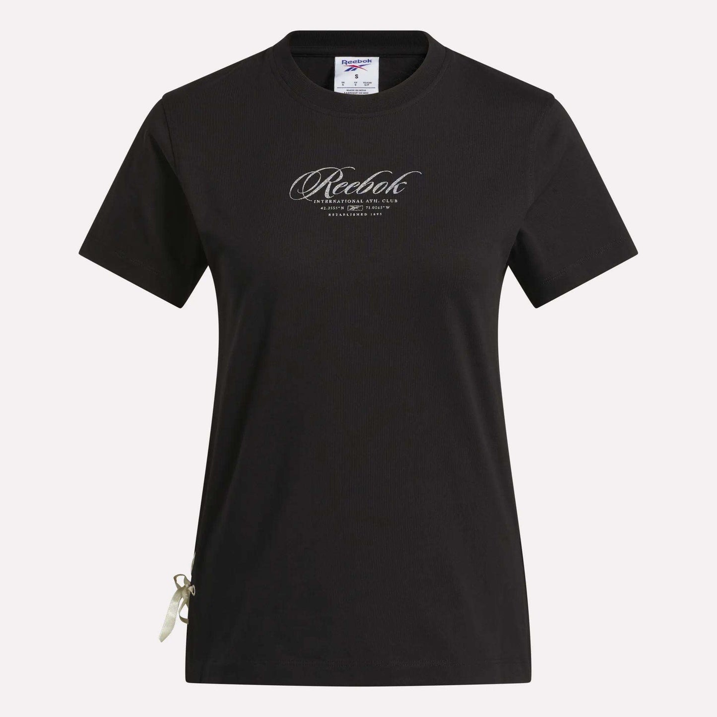 The Reebok Women's Ribbon T-Shirt is shown in black with short sleeves against a white background. It features the brand’s cursive logo on the chest and a small ribbon detail at the bottom left hem. Made from soft cotton, this t-shirt offers comfortable wear and metallic shine for a stylish everyday look.
