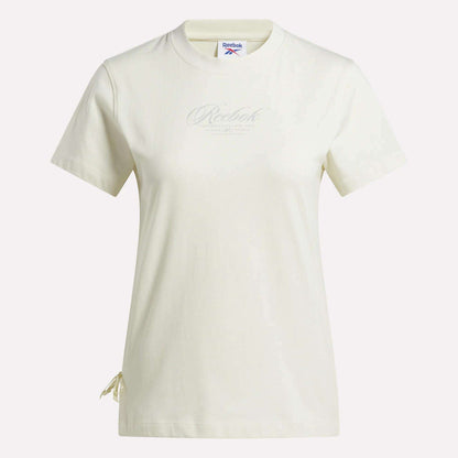 The Reebok Women's Ribbon T-Shirt is a cream-colored, relaxed fit short-sleeve top featuring a subtle chest logo and an adjustable drawstring detail near the left hem.