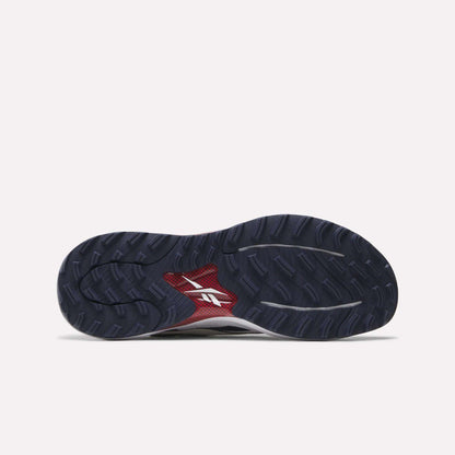 The image shows the sole of the Reebok Nano Golf Shoes, featuring a black and dark blue tread pattern with a white logo over a red section in the center.
