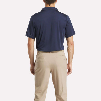 A man faces away, wearing a Reebok Men's Crushers GC Replica Polo in navy blue, tucked into light beige pants against a plain white background.