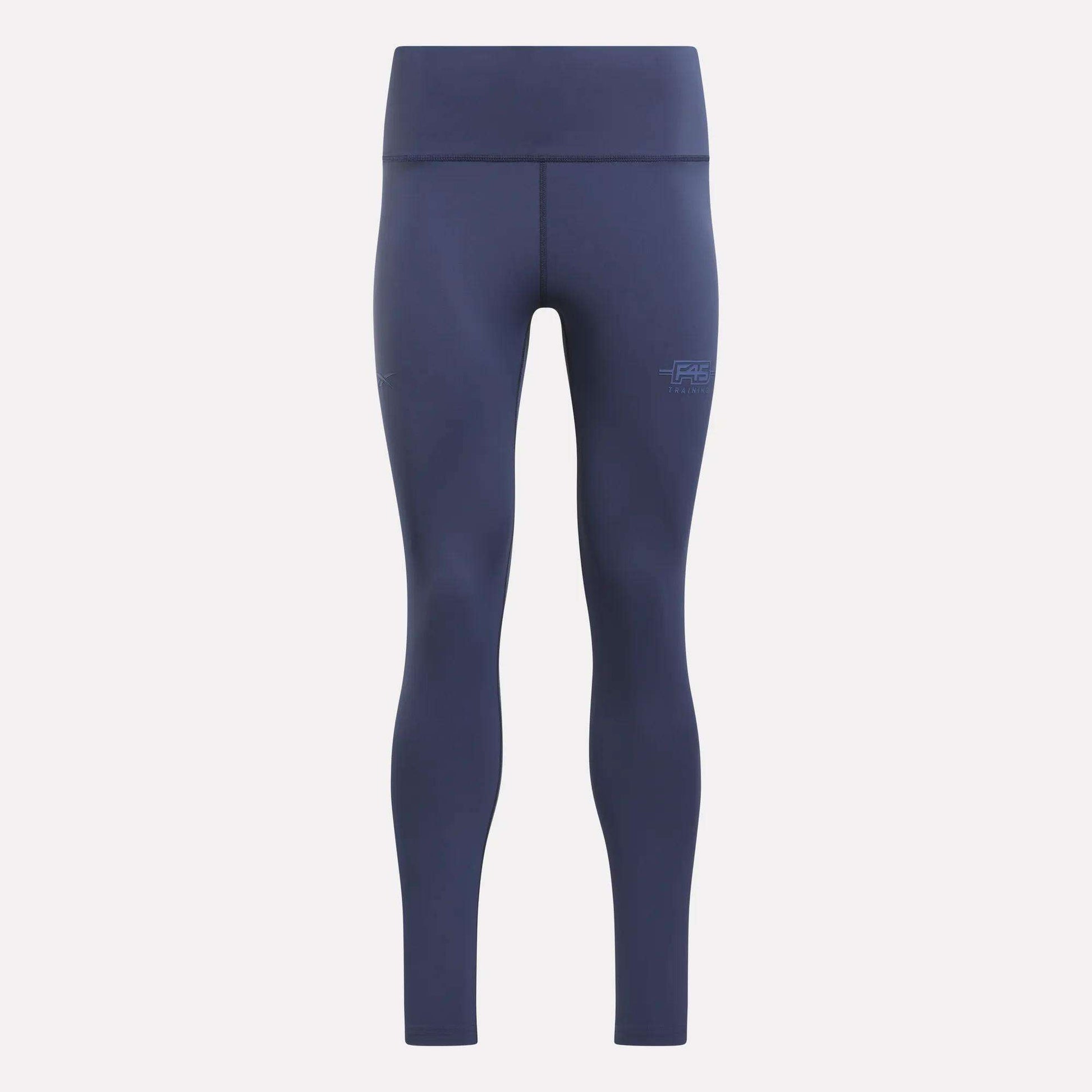 The Women's Reebok x F45 Training Leggings by Reebok are navy blue, high-waisted athletic leggings with a supportive high-rise waistband and a seamless design. They feature visible stitching and a small F45 logo on the left thigh, and are displayed against a plain light background.