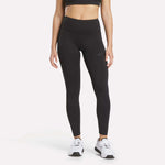 A woman is wearing a black sports bra, Women's Reebok x F45 Training Leggings in black by Reebok, and white sneakers, standing against a plain white background. Her face is not visible in the image.