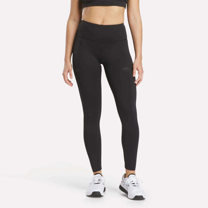 A woman is wearing a black sports bra, Women's Reebok x F45 Training Leggings in black by Reebok, and white sneakers, standing against a plain white background. Her face is not visible in the image.