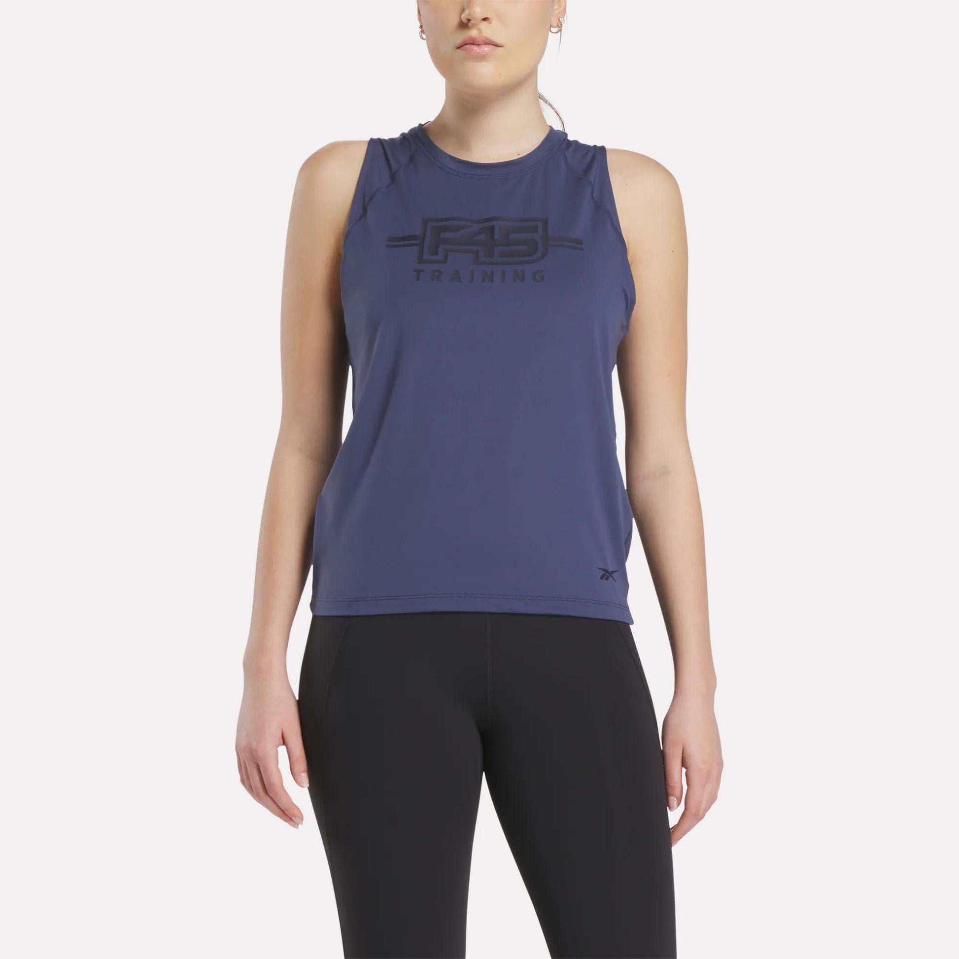 A woman wears the Women's Reebok x F45 Training Tank Top in navy and black leggings, standing facing forward against a plain white background.