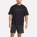 A man wears the Reebok x F45 Training Tonal Graphic T-Shirt in black and black athletic shorts featuring a small Reebok logo on the left leg.