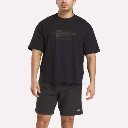 A man wears the Reebok x F45 Training Tonal Graphic T-Shirt in black and black athletic shorts featuring a small Reebok logo on the left leg.