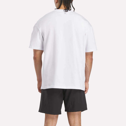 A person is standing and facing away from the camera, wearing a plain white Reebok x F45 Training Relaxed T-Shirt and black shorts against a light background.