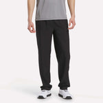 A person wearing a gray short-sleeve shirt, Men's Reebok x F45 Training Woven Pants in Vector Navy, and white athletic shoes stands against a plain white background. Their outfit is ideal for high-intensity training or F45 Training sessions, with the Reebok pants providing reliable comfort and support. Their face is not visible.