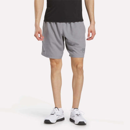 A person in a black shirt, Men's Reebok x F45 Training Woven Shorts (gray), and white running shoes stands against a plain white background, shown from shoulders to feet—ready for intense workouts or F45 Training.