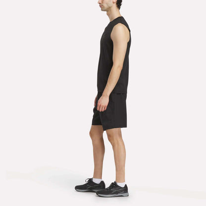 A man stands in profile view against a plain white background, wearing the Reebok x F45 Training Tank Top for men—perfect for high-intensity workouts or an F45 Training session. He pairs it with black shorts and black athletic shoes with white soles.