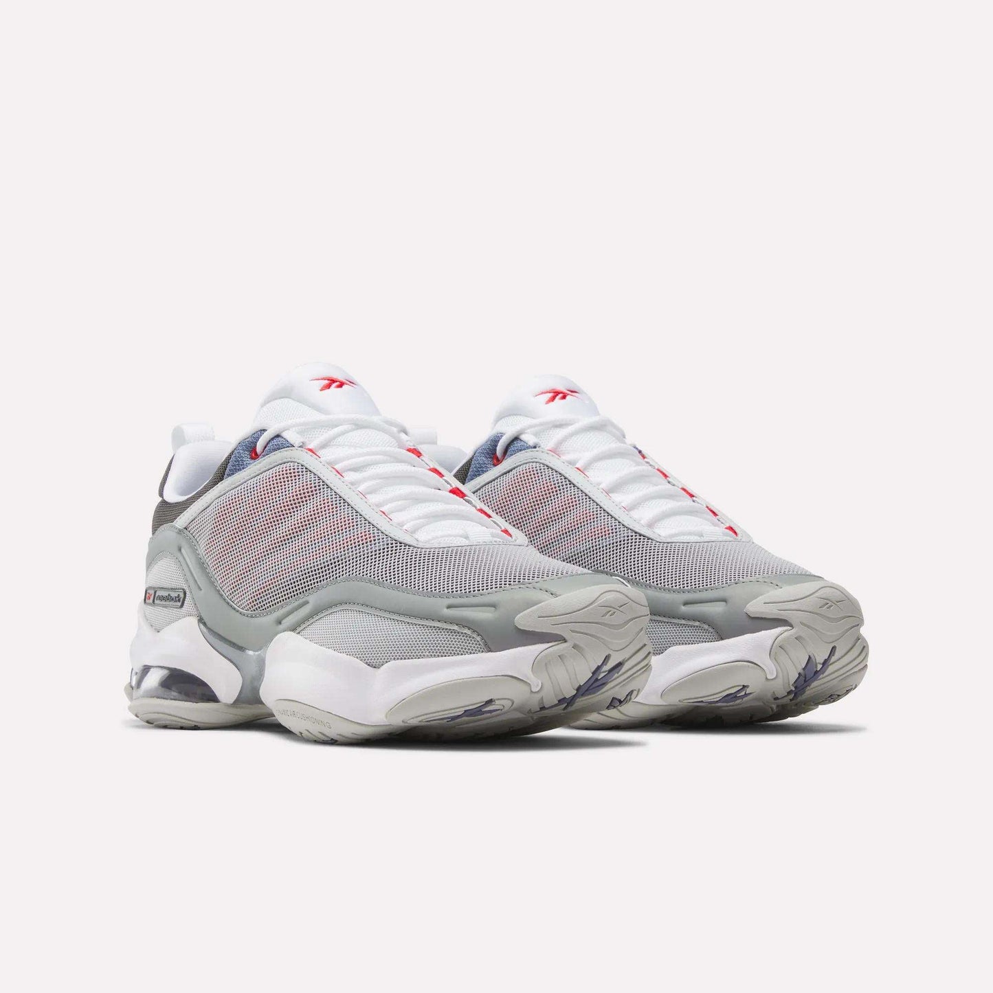 A pair of Reebok DMX Series 3000 Shoes in white, gray, and red with mesh uppers, chunky soles featuring DMX moving air technology for enhanced comfort, and prominent Reebok branding, displayed side by side on a light background.