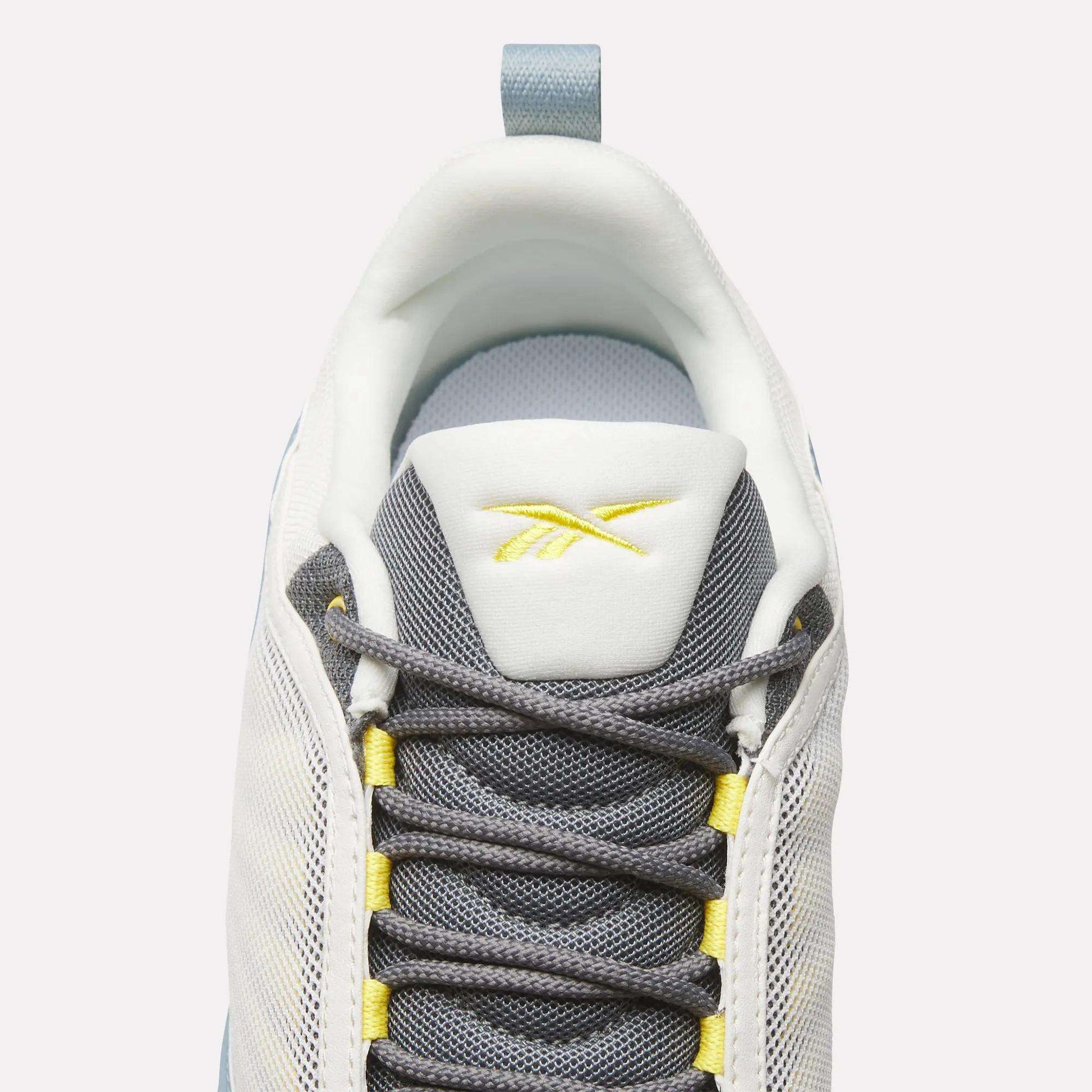Top view of Reebok DMX Series 3000 Shoes in white and grey with yellow accents, dark grey laces, DMX moving air technology for comfort, and a yellow Reebok logo on the tongue, set against a light background.