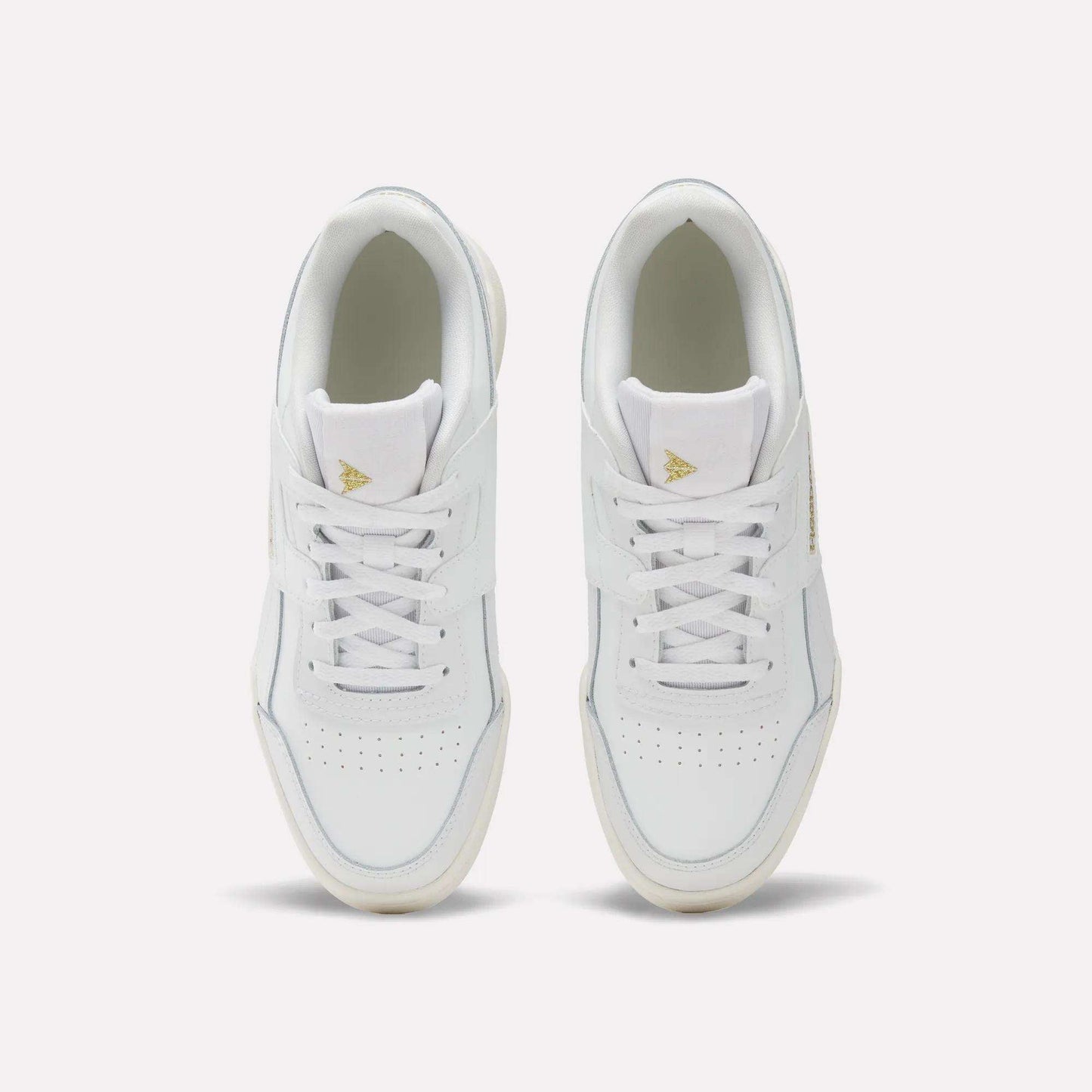 A pair of Reebok Workout Plus Shoes for big kids with laces, seen from above on a light background. These sporty white sneakers have perforated toe boxes and gold triangle logos on the tongues—ideal for juniors who want style and comfort.