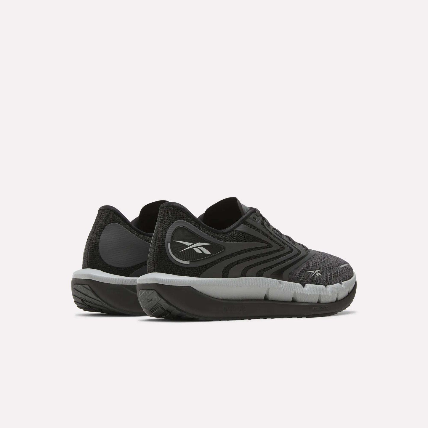 A pair of Reebok Men's FloatZig Tread Running Shoes in black and gray with white soles and a cushioned midsole are placed side by side on a light background—ideal for treadmill workouts.