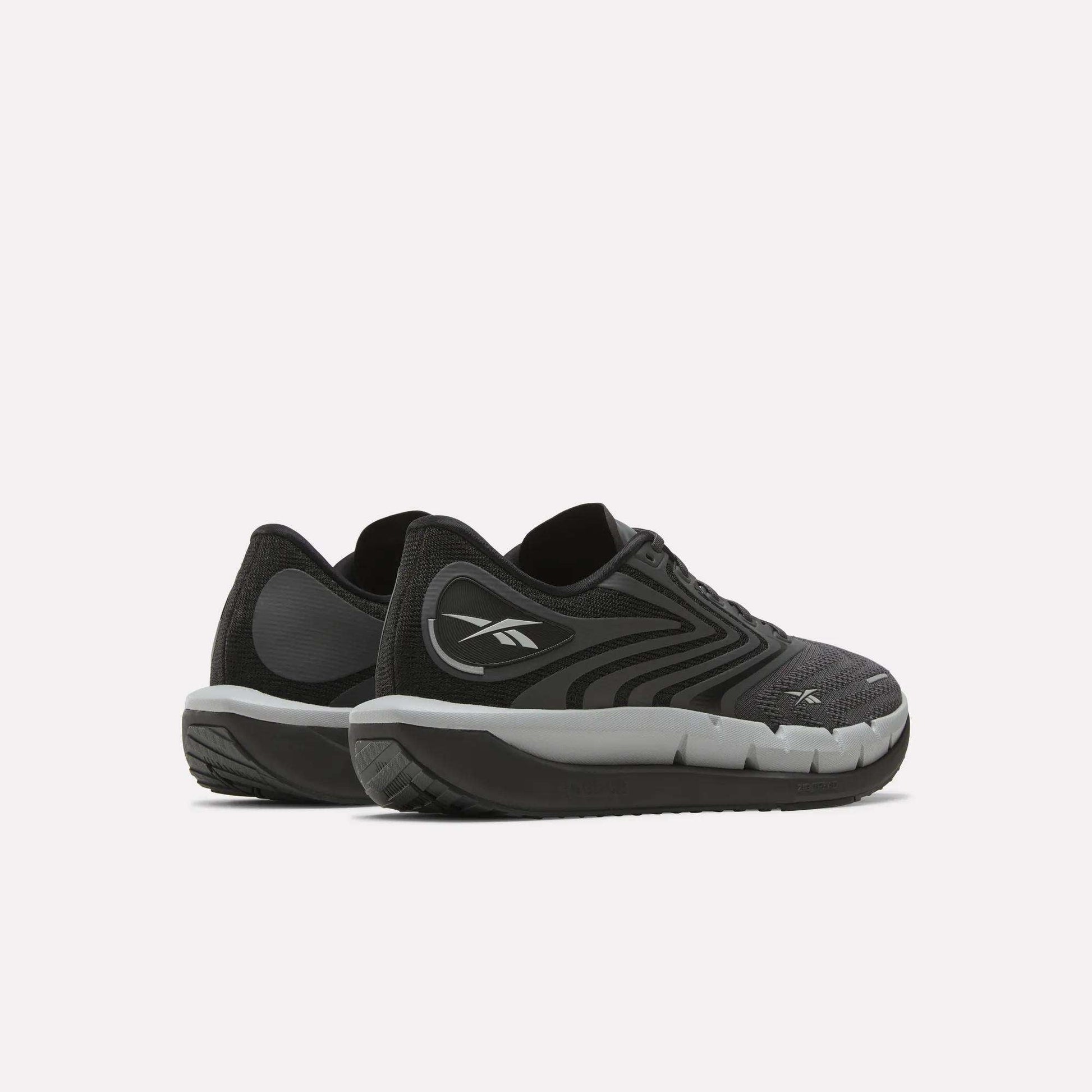 A pair of Reebok Men's FloatZig Tread Running Shoes in black and gray with white soles and a cushioned midsole are placed side by side on a light background—ideal for treadmill workouts.