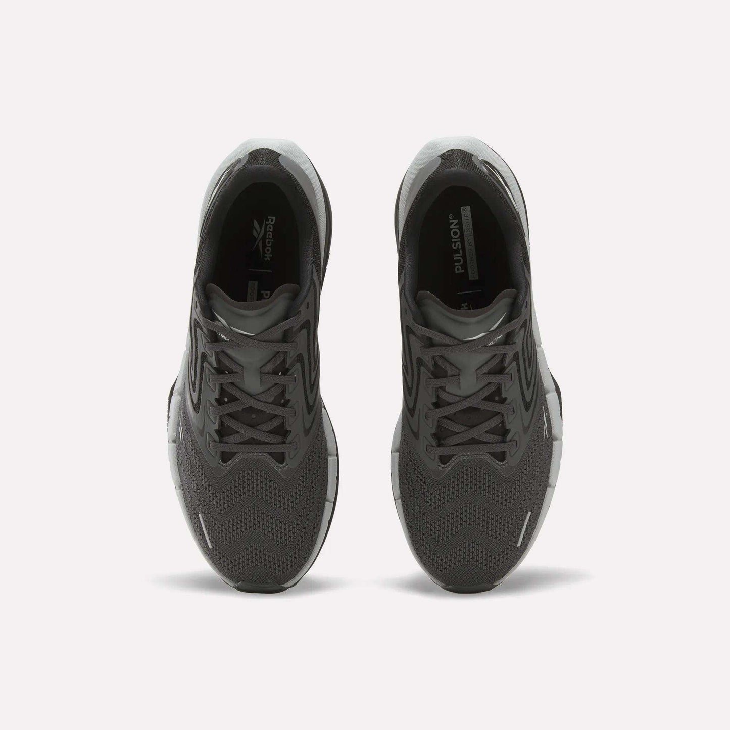 A pair of Men’s FloatZig Tread Running Shoes by Reebok in black, seen from above with laces, mesh uppers, and branded tongue. Cushioned midsoles make them ideal for treadmill workouts. Placed side by side on a plain white background.