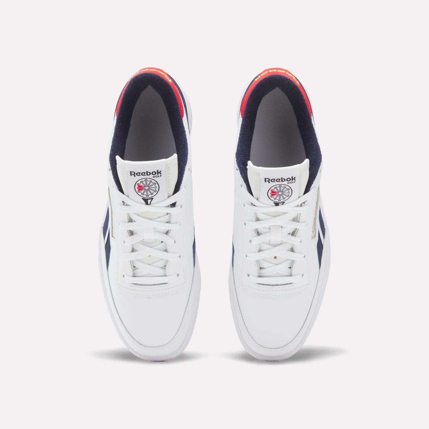A top view of Reebok Men's Club C Revenge Golf Shoes in white with navy accents, red heel detail, and a spikeless outsole. Water-resistant shoes feature the Reebok logo and a basketball graphic on each tongue.