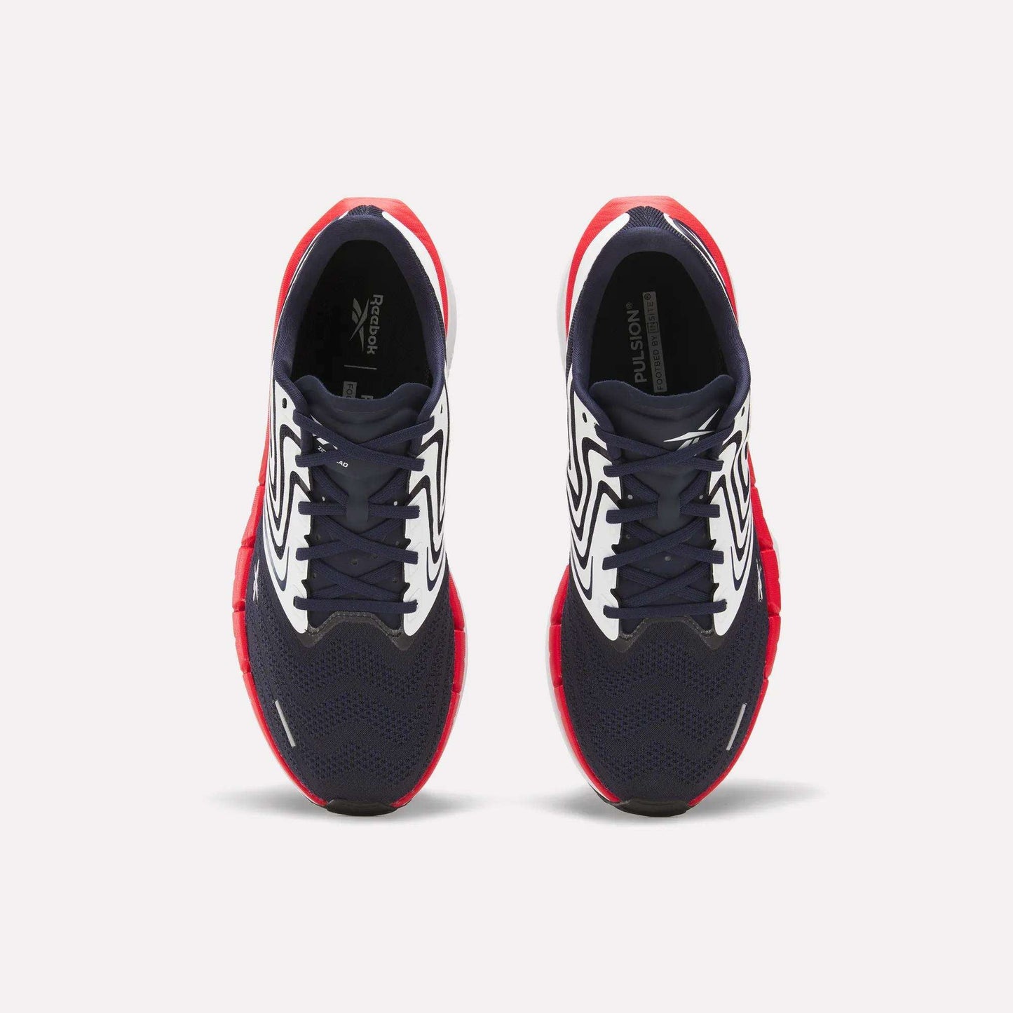 The Reebok Men's FloatZig Tread Running Shoes feature navy blue mesh toes, white patterned sides, and bright red soles—ideal for treadmill workouts. Shown from above against a plain white background.