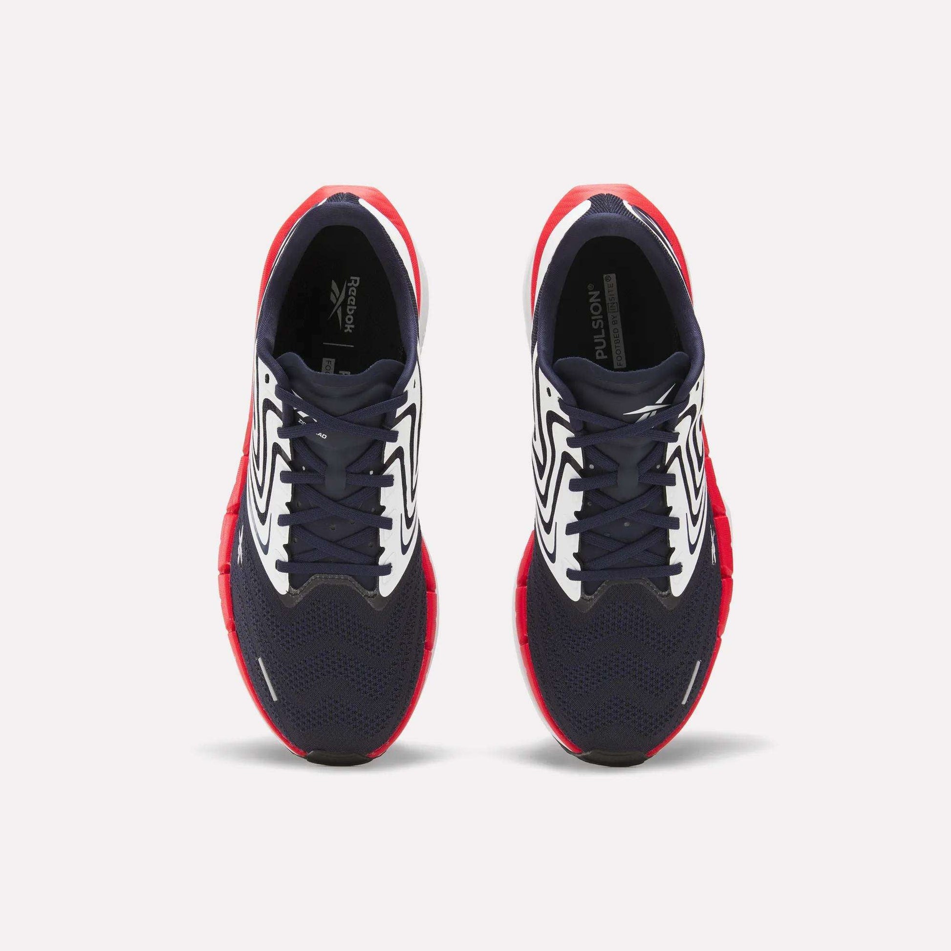 The Reebok Men's FloatZig Tread Running Shoes feature navy blue mesh toes, white patterned sides, and bright red soles—ideal for treadmill workouts. Shown from above against a plain white background.