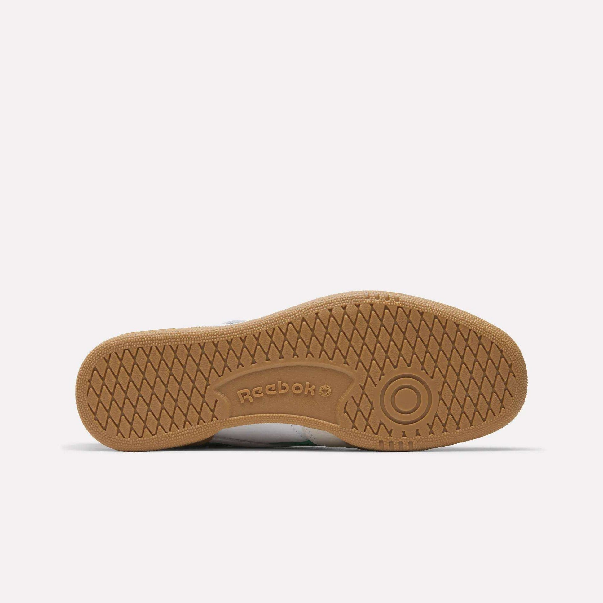 The image shows the bottom sole of the Reebok Men's Club C Revenge Vintage Shoes, featuring a tan rubber surface with a herringbone tread pattern and embossed Reebok branding, underscoring its classic heritage style.