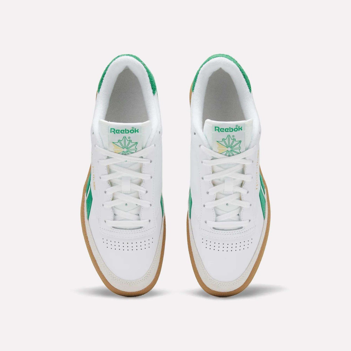 Top view of a pair of Reebok Men's Club C Revenge Vintage Shoes in white, featuring green accents, heritage branding on the tongue, and gum soles, placed side by side on a plain light background.