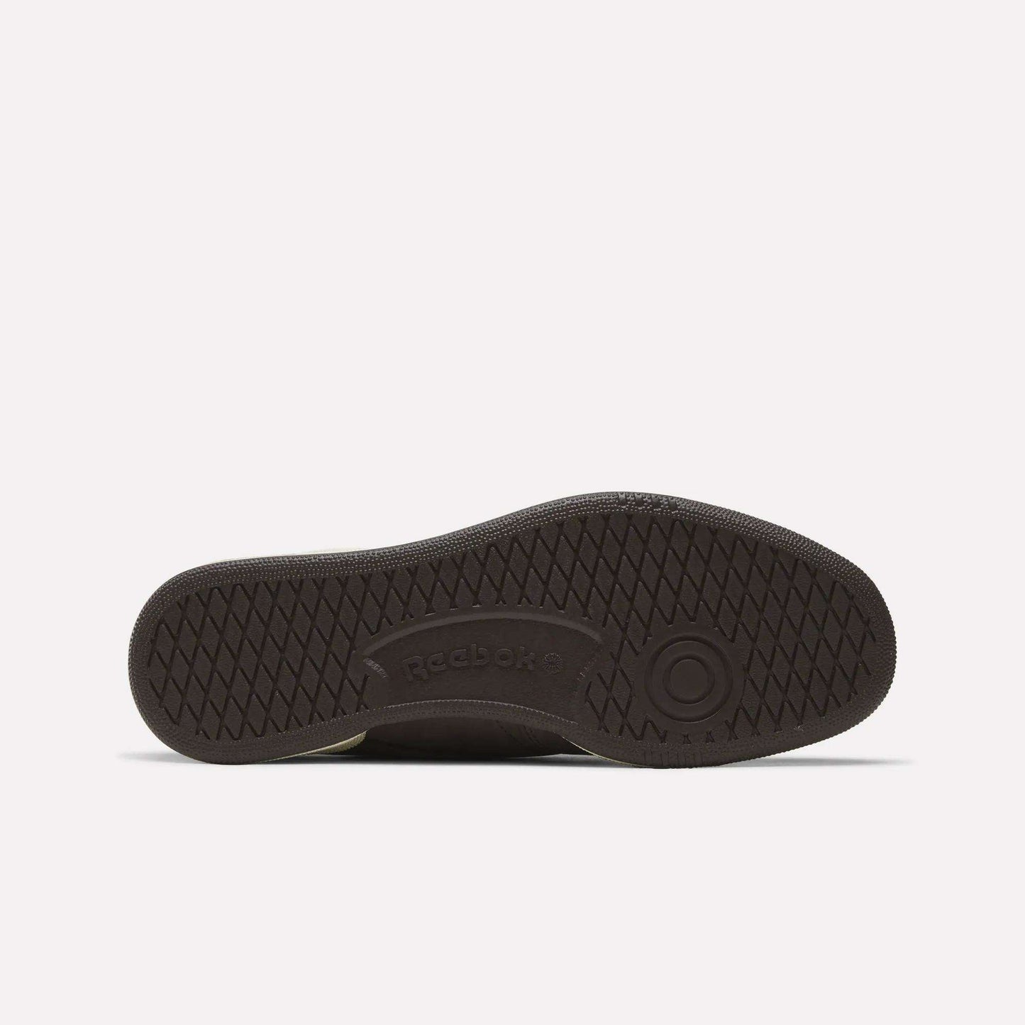 The image shows the sole of a dark Men's Club C 85 Shoe by Reebok, featuring a textured crisscross pattern, a circular toe design, and the embossed Reebok logo at the center.